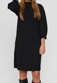 Svart texturerad klänning med hög halsringning, lösa trekvartsärmar och sidoklyfta, tillverkad av ett vävt tyg i rutmönster.