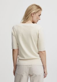Lys beige kortærmet striktrøje med rund halsudskæring og subtil tekstur, kombineret med lyse bukser. Enkel design uden mønstre.