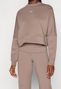 Sweatshirt marron cropped en tissu doux, avec un col rond et un petit logo Nike blanc sur la poitrine ; accompagné d'un pantalon assorti.