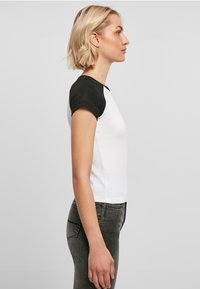 Kortermet T-skjorte med hvit kropp og svarte raglan-ermer, med rund hals og rett passform, sammen med grå jeans.