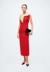 Red sleeveless dress with a plunging neckline and fitted silhouette. Black clutch in hand and pointed heels complete the look.