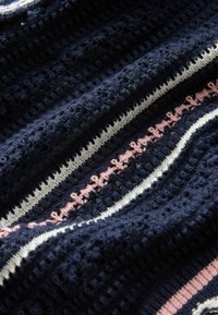 Tissu tricoté bleu foncé avec un motif texturé, présentant des rayures horizontales blanches et roses et de petits détails en boucle à l'intérieur de la rayure rose.