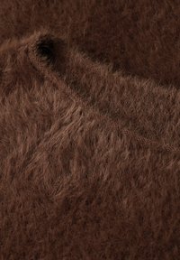 Nahaufnahme eines weichen, flauschigen braunen Stoffs mit einer Naht und einem Knopfloch-Detail auf der strukturierten Oberfläche.