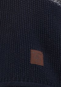Berretto di lana lavorato a maglia di colore navy con texture a coste. Dotato di un'etichetta in pelle marrone con la scritta "KEY LARGO" e un emblema.