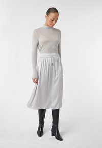 Haut à manches longues gris clair avec col roulé, associé à une jupe fluide gris clair avec une taille élastique et un cordon de serrage. Bottes noires montantes.