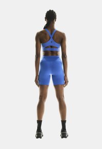 Plavi sportski crop top i kratke hlače set. Sadrži izrez na leđima i teksturiranu tkaninu. Nositi sa crnim sportskim čarapama i cipelama.