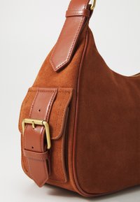 Braune Wildlederhandtasche mit einem glatten Ledergriff, goldener Schnalle und detaillierter Klappe. Abgerundete Form mit einer weichen Textur.