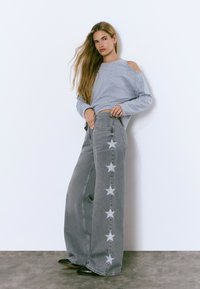 Gray oversized long-sleeve top, gray wide-leg jeans with white star patterns along the side, paired with black pointy shoes.