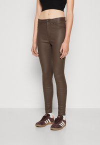 Brune imiterte skinn skinny jeans med en glatt finish og subtile sømdetaljer, kombinert med mørke sneakers med hvite striper.