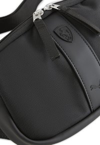 Borsa accessoria nera realizzata in tessuto testurizzato con dettagli lisci. Presenta due cerniere in argento e una patch con il logo. Design compatto ed elegante.