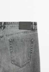 Dos d'un jean en denim gris montrant une poche unique et un patch en cuir noir avec la marque "Massimo Dutti."