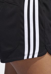 Pantalones cortos atléticos negros con una textura suave, bolsillos laterales y tres franjas blancas a lo largo de las costuras exteriores para crear contraste.