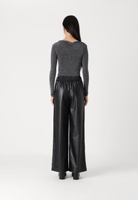 Top grigio fitted a maniche lunghe con scollatura a barca abbinato a pantaloni neri in eco-pelle a gamba larga con elastico in vita.