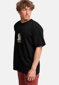 Sort bomulds t-shirt med korte ærmer, der har et farverigt grafisk print på forsiden. Lige snit, minimal struktur og afslappet pasform.