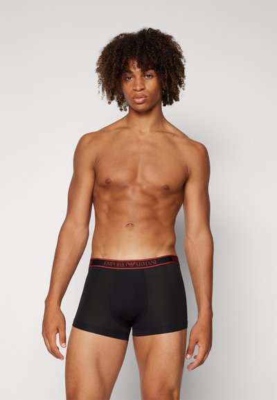 Boxer neri con elastico rosso "Emporio Armani", caratterizzati da una vestibilità classica e tessuto liscio, indossati da una persona senza maglietta.