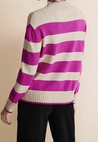 Person klädd i en beige och ljusrosa randig polotröja i kombination med svarta byxor, sedd bakifrån.