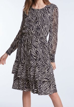 Nainen, jolla on pitkähihainen polvipituinen mekko mustavalkoisella seeprakuvioinnilla ja kerroksellinen röyhelöhelma.