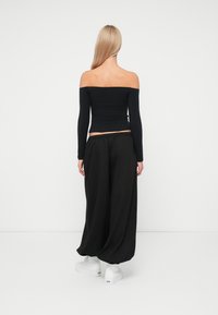 Μαύρη μπλούζα off-shoulder με μακριά μανίκια, συνδυασμένη με χαλαρούς μαύρους παντελόνους και λευκά sneakers, διαθέτοντας χαλαρή εφαρμογή και απλό σχέδιο.