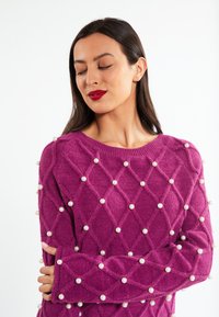 Fuchsia strikket sweater med diamantmønster, pyntet med hvide perler. Rund halsudskæring og lange ærmer. Blød tekstur, hyggelig pasform.