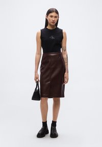 Μαύρο αμάνικο τοπ με λογότυπο, καφέ δερμάτινη midi φούστα, μαύρη τσάντα χειρός, μαύρες κάλτσες και χοντρά μαύρα παπούτσια. Λείες υφές και εφαρμοστό σχέδιο.