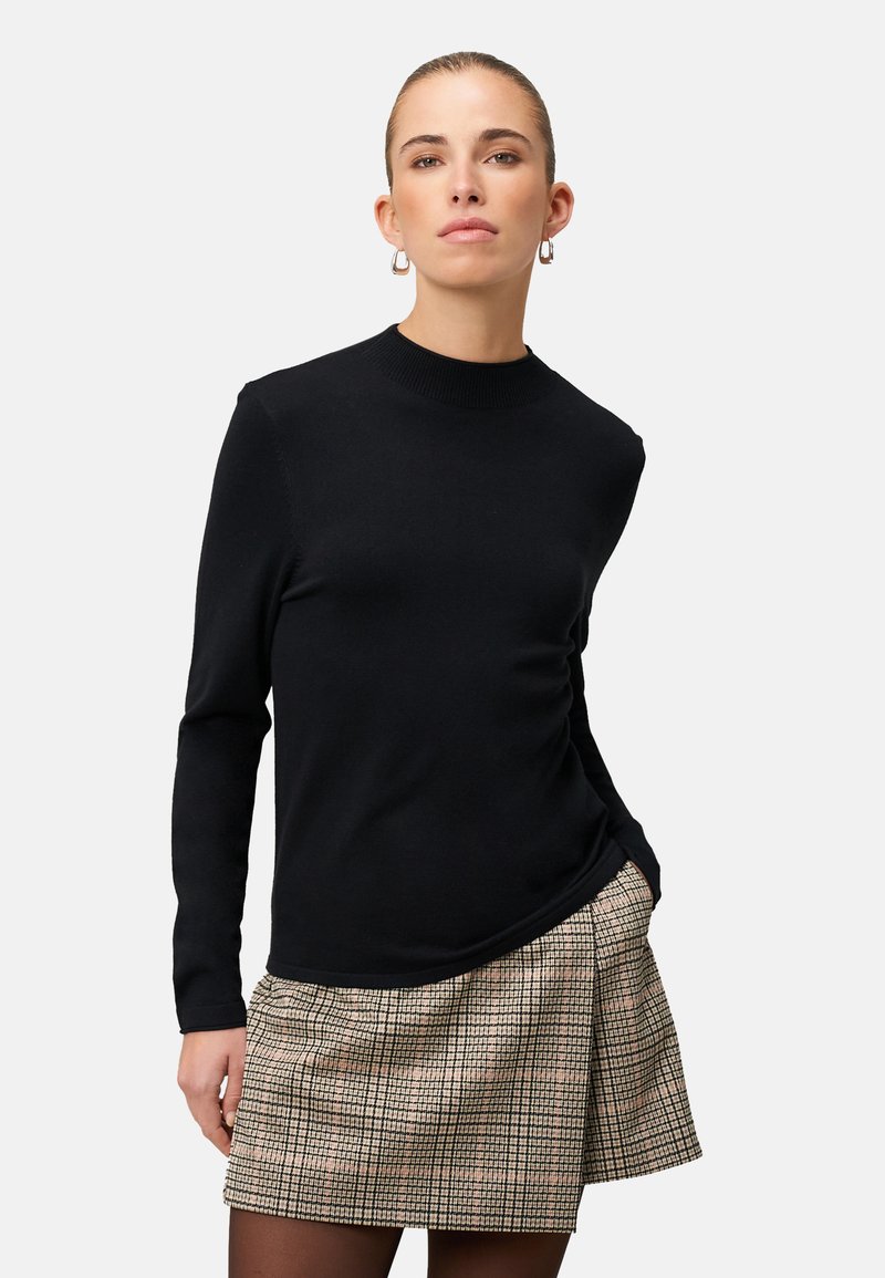 Maglione nero a maniche lunghe con scollo rotondo, abbinato a una gonna a quadri. Il tessuto del maglione appare liscio; la gonna presenta un motivo a quadretti texturizzato.