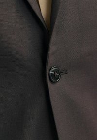 Dunkelbrauner Blazerstoff mit strukturiertem Gewebe, ausgestattet mit einem schwarzen Kunststoffknopfdetail auf der Vorderseite. Das Innenfutter ist in einer helleren Farbe gehalten.