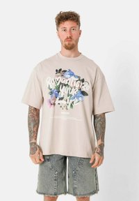 Lichtbeige oversized t-shirt van katoen met een grafisch ontwerp van bloemen en tekst. Gecombineerd met lichtblauwe denimshorts met ritsen.