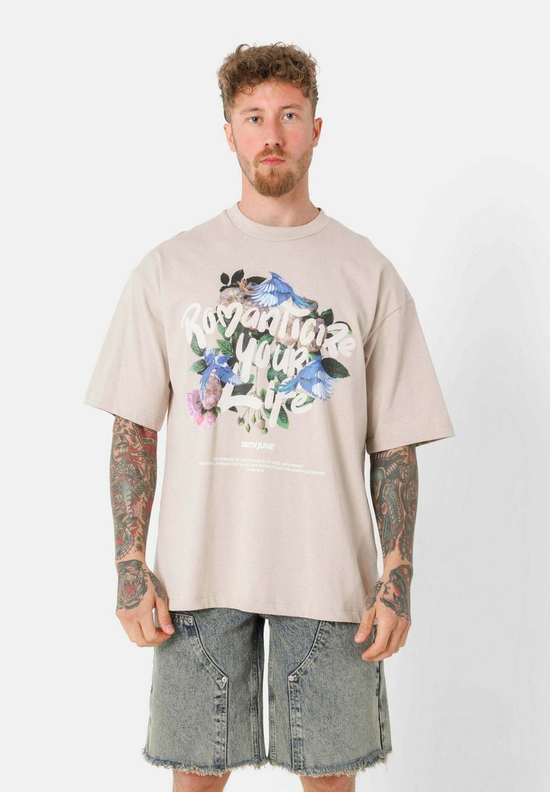 Lichtbeige oversized t-shirt van katoen met een grafisch ontwerp van bloemen en tekst. Gecombineerd met lichtblauwe denimshorts met ritsen.
