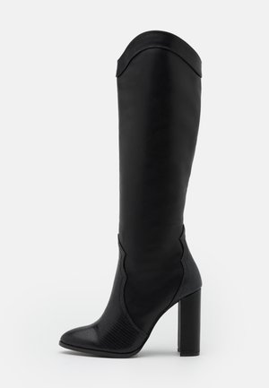 Botte noire montante à talon avec un bout arrondi et pointu, une partie inférieure texturée, une tige supérieure lisse et un bord supérieur courbé.