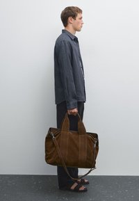 Brown suede bag with double handles and a removable shoulder strap. Features visible stitching and a soft texture.