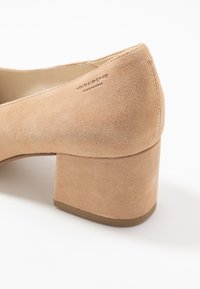 Beige mockasklackskor med rund tå och slät yta. Inuti har de en tan-färgad foder och ett präglat märke på baksidan.
