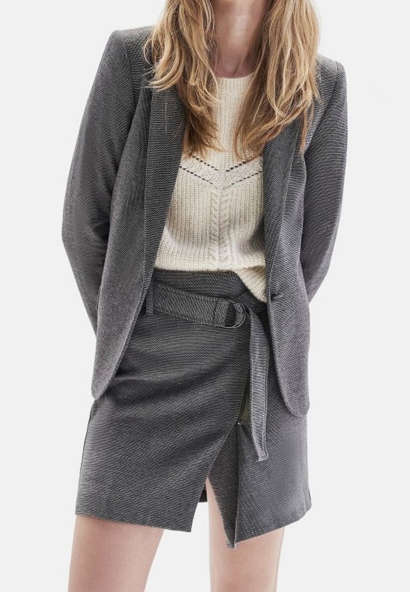 Szary żakiet z teksturowanym wzorem, w połączeniu z dopasowaną spódnicą z paskiem w talii i rozcięciem z przodu. Pod spodem beżowy sweter dziany.