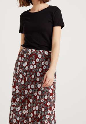 Chemise noire à manches courtes associée à une jupe bordeaux à motif floral avec des fleurs blanches et noires. La jupe présente une coupe fluide.