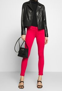 Chaqueta de cuero negra estilo biker, suéter negro ajustado de cuello alto, jeans pitillo rosas, bolso negro con hebilla y tacones negros con tiras.
