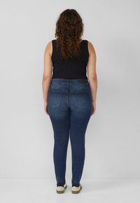 Dunkelblaue Skinny Jeans aus Denim mit glatter Textur, die zwei Gesäßtaschen und einen Bund mit einem schwarzen Etikett verfügen.