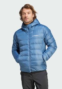 Chaqueta azul aislante con capucha, que presenta un diseño acolchado, cremallera frontal y logo en el pecho izquierdo. Textura de tela suave y brillante.