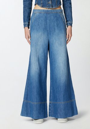 Jeans en denim à jambes larges avec un délavage bleu clair, dotés d'une taille haute, d'un ourlet brut, et d'une couture contrastée subtile. Texture douce et coupe décontractée.
