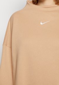 Överdimensionerad beige sweatshirt med hög halsringning, utrustad med en vit Nike swoosh-logotyp på bröstet och mjukt, texturerat tyg.