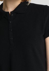 Polo noir avec col, manches courtes et patte de boutonnage sur le devant. La texture du tissu semble lisse et douce.