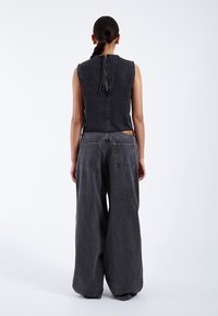 Black denim jumpsuit with wide-leg trousers, sleeveless design, back zip closure, and a textured finish. Features two back pockets.