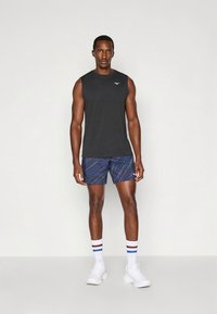 Męski strój sportowy z czarną koszulką bez rękawów oraz niebieskimi szortami z wzorem i wielokolorowymi paskami. Białe buty i skarpetki.