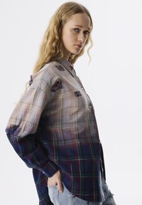 Button-up shirt met een geruit patroon in tinten van blauw, rood en grijs. Heeft versleten details en een losse pasvorm. Lichtgewicht stof.