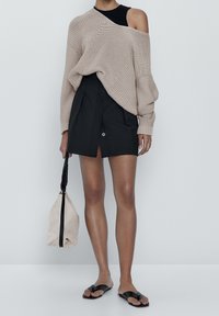 Beige neuleva oversized neule, musta istuva hame etupainikkeella, mustat litteät sandaalit ja beige teksturoitu laukku mustalla hihnalla.