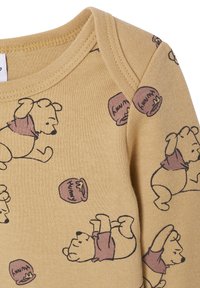 Gelbes Gewebe mit sich wiederholenden Illustrationen eines Bären und Honigtöpfen. Weiche, glatte Textur mit Rundhalsausschnitt und genähtem Kragen.