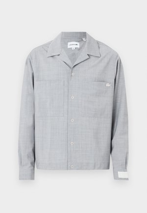 Szara koszula zapinana na guziki z teksturowanej tkaniny, z dwiema kieszeniami na piersi, ostrym kołnierzykiem i małym logo po lewej stronie. Długie rękawy z mankietami.