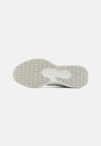 Hvid sneakersål med tekstureret mønster for greb, der har et centralt logo. Materialet ser ud til at være gummi, designet til trækkraft og holdbarhed.