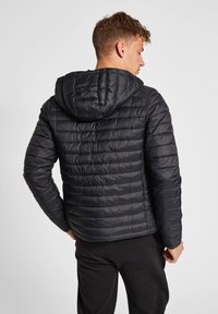 Sort puffjakke med hætte, der har et quiltet design og en glat tekstur. Ærmerne er tætsiddende, og den har en indsnævret talje.