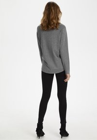 Maglione grigio a maniche lunghe con una vestibilità comoda, abbinato a jeans skinny neri e stivali alla caviglia con dettagli arricciati.