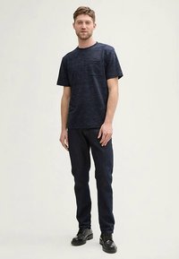Marineblå kortærmet T-shirt med subtil tekstur, kombineret med mørke jeans. Model iført sorte snørestøvler. Enkel og tætsiddende design.
