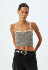 Afskåret top i ternet mønster med blondekant, der har tynde stropper. Bæres med højtaljede sorte jeans og en stor sølvbæltespænde.